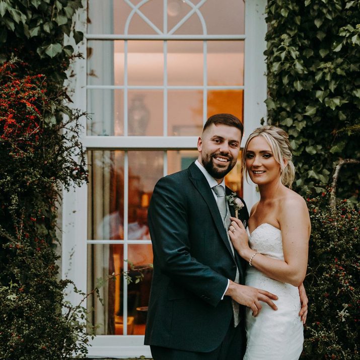 A smiling bride and groom standing outside a window at Wooladon Estate