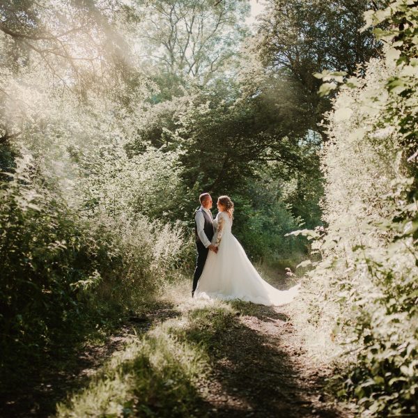 A bride and groom standing surrounded by bushes and trees in one of Wooladon Estates country woodland lanes