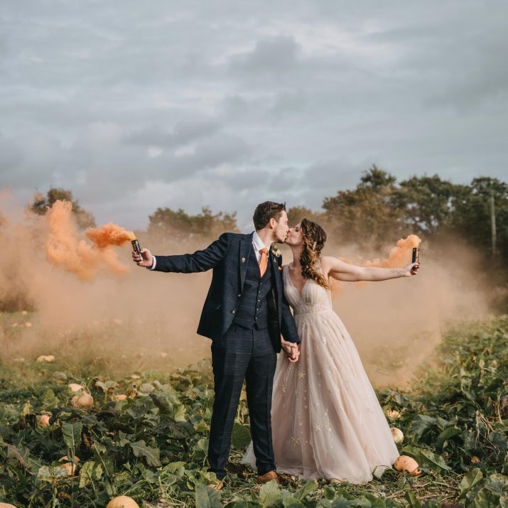 A newly married couple kissing in the pumpkin patch at Wooladon Estate as they hold orange smoke canisters