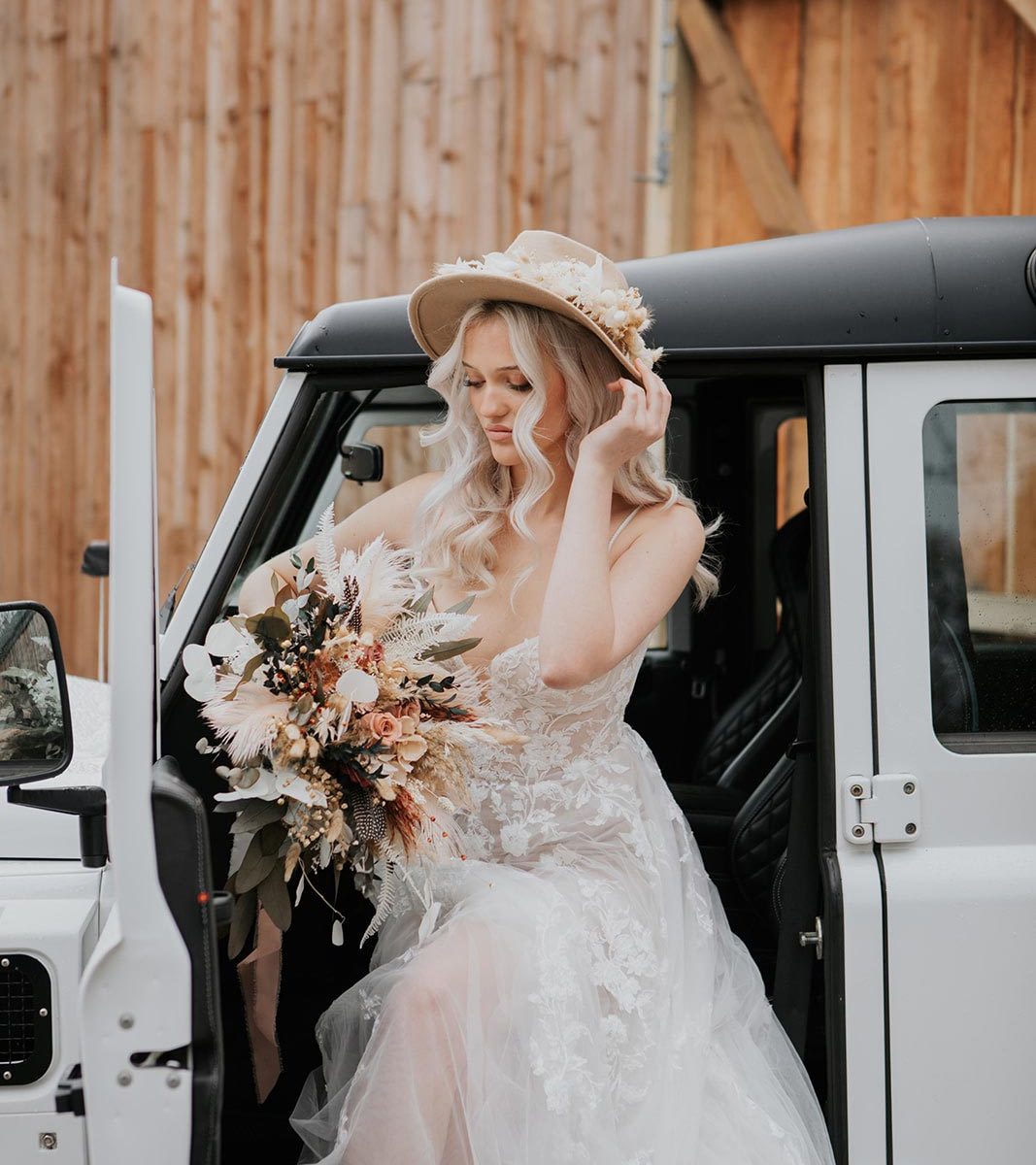 A bride stepping out of a Land Rover in front of the barn at Wooladon Estate