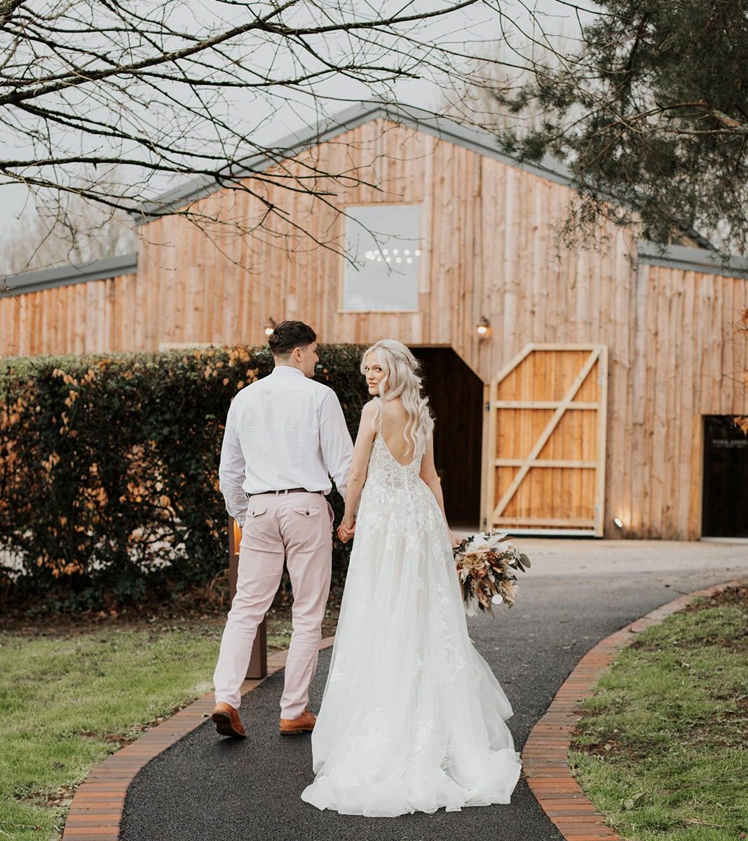 A newlywed couple walking along the path toward the barn at Wooladon Estate