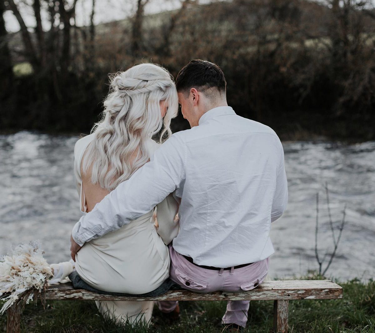 A newlywed couple sit together on a bench by a river on Wooladon Estate